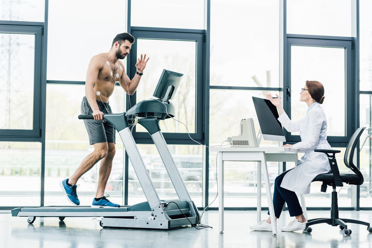 doctor sitting at computer desk and conducting endurance test with sportsman in gym